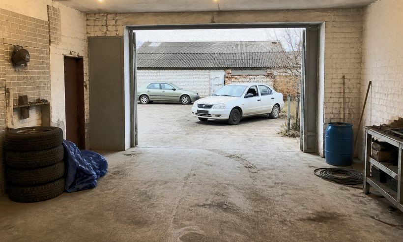 Вид из бокса через открытые ворота: на бетонной площадке стоят два обычных старых легковых автомобиля